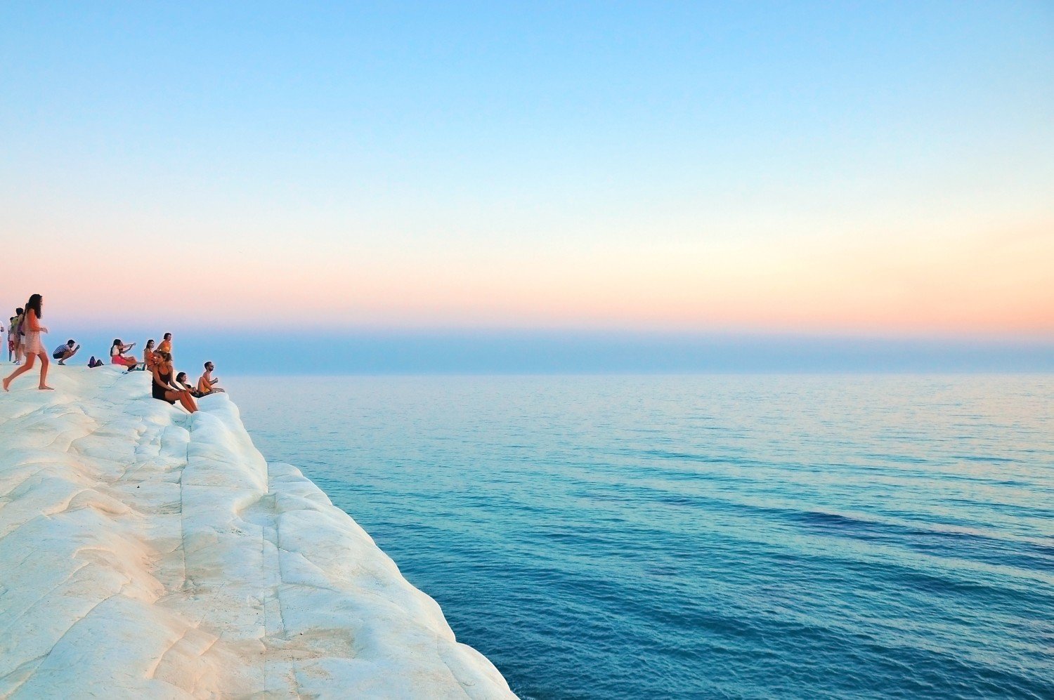 A breathtaking view from a cliff with people standing on a glacier and sitting by the edge of the ocean. The horizon blends shades of blue and pink, symbolizing the journey ahead—one of personal transformation and new opportunities.