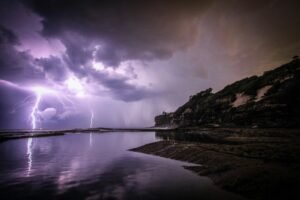 Lightning striking over a calm beach with dark clouds and a cliff, symbolizing conflict and tension in storytelling.